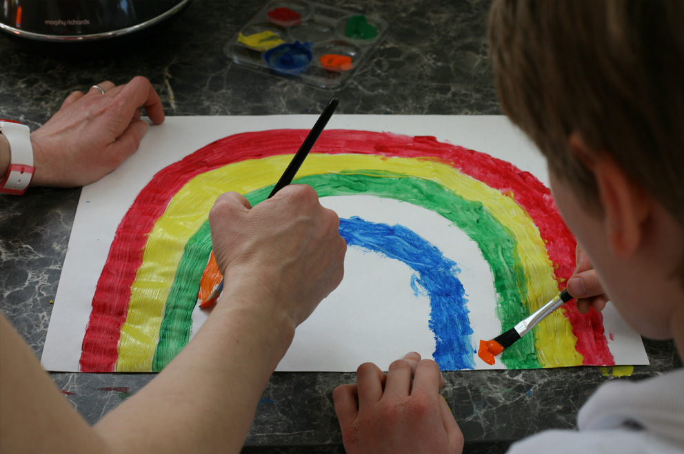 Zwei Kinder malen mit Tusche einen Regenbogen.