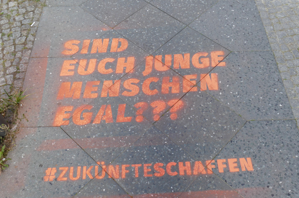 Schriftzug in Sprühkreide auf Gehweg vor Bundesjugendministerium: "Sind Euch junge Menschen egal" und #Zukünfteschaffen