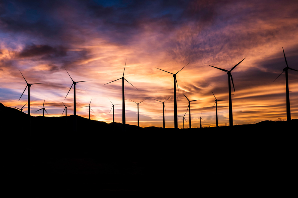 Foto einer Reihe von Windrädern im Sonnenuntergang.