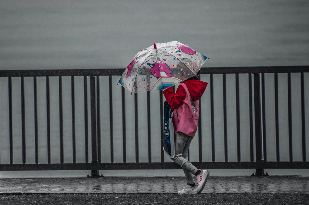 Ein Kind schützt sich mit einem Regenschirm vor Regen.