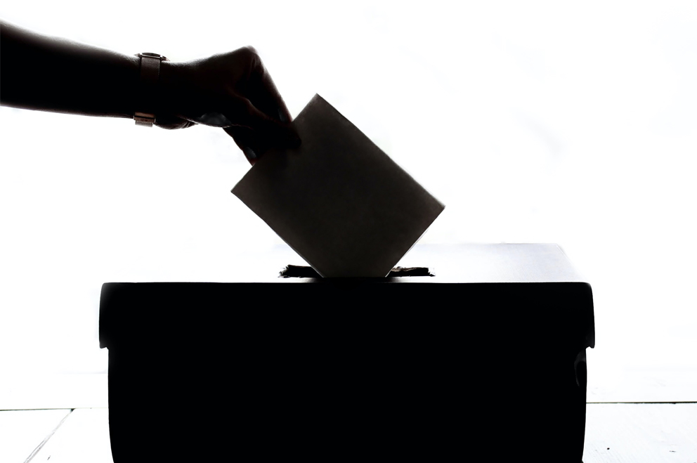 Eine Hand wirft einen Wahlzettel in eine Box. 