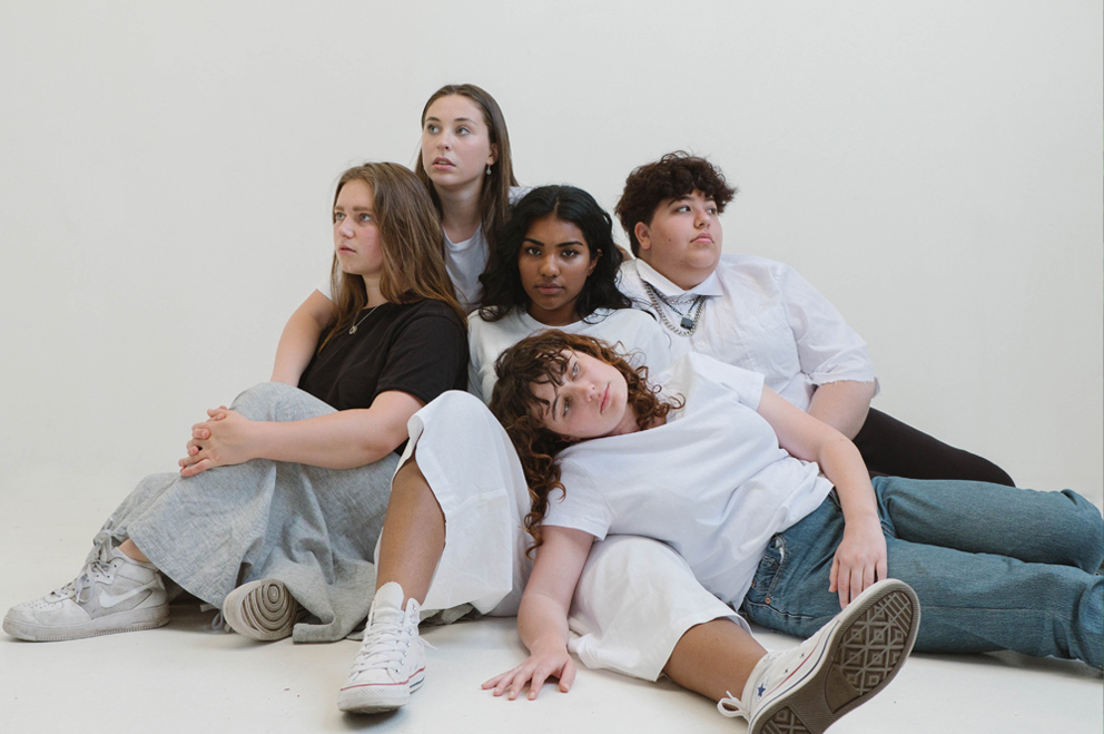 Fünf Jugendliche sitzen eng beieinander auf dem Boden und blicken in die Kamera.