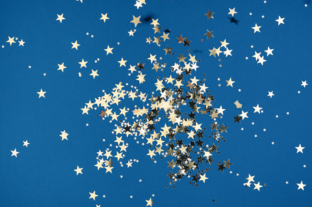 Konfetti aus glänzenden Sternen vor blauem Hintergrund.