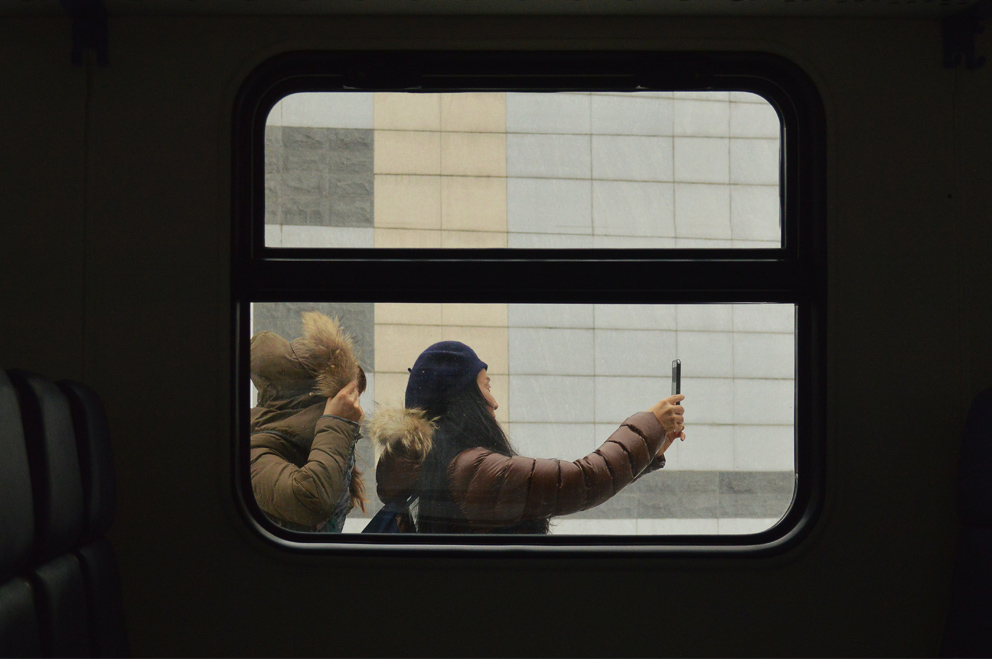 Bild aus einem Zugfenster nach draußen, wo zwei junge Frauen ein Selfie machen.