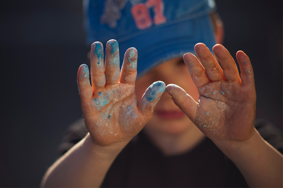 Ein kleines Kind streckt seine Hände aus. An den Fingern blaue Kreidereste.