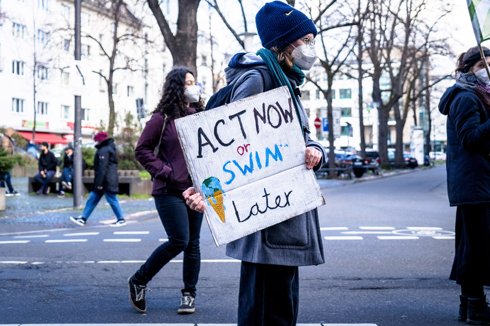 Eine Person trägt ein Transparent mit der Aufschrift: Act now or swim later