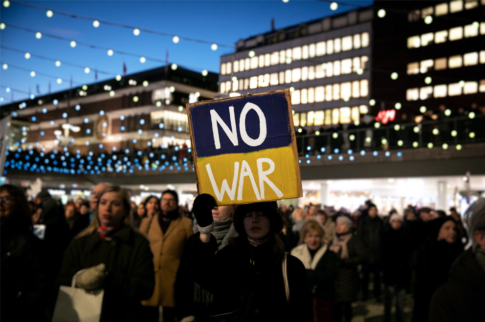 Eine junge PErson hält ein blau-gelbes Plakat, auf dem steht: "No War"