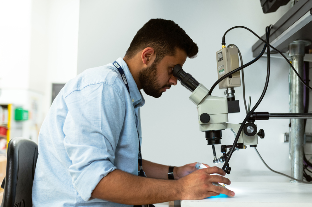 Foto eines jungen Mannes, der ein Mikroskop benutzt.