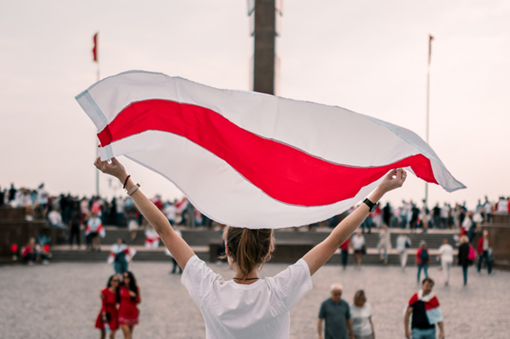 Eine junge Person hält eine Flagge von Belarus in die Höhe.